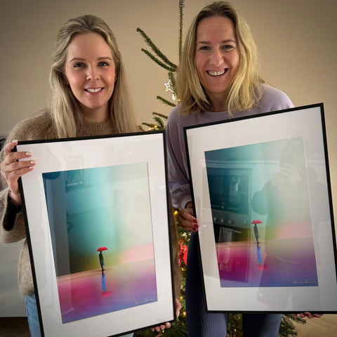 Two women collectors each hold a framed Limited Edition Print by colorblind contemporary artist Kalle Hellzén