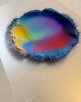 IMPACT 0016, angled view of the full disc showing a yellow wedge at left, a red band low in the centre, and a blue-to-navy ring, bordered by a ragged blue-black fringe of fine printed threads.