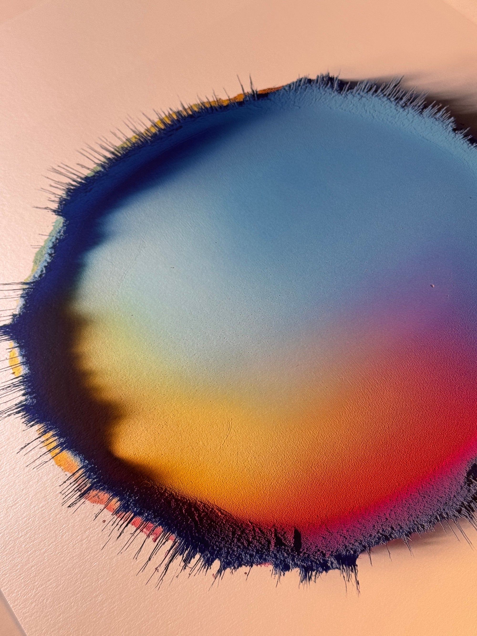 IMPACT 0017, angled view of the full disc: blue across the upper area sliding to amber and orange-red at lower left, bordered by a ragged navy fringe of fine threads, on cream metallic paper.