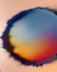 IMPACT 0017, angled view of the full disc: blue across the upper area sliding to amber and orange-red at lower left, bordered by a ragged navy fringe of fine threads, on cream metallic paper.