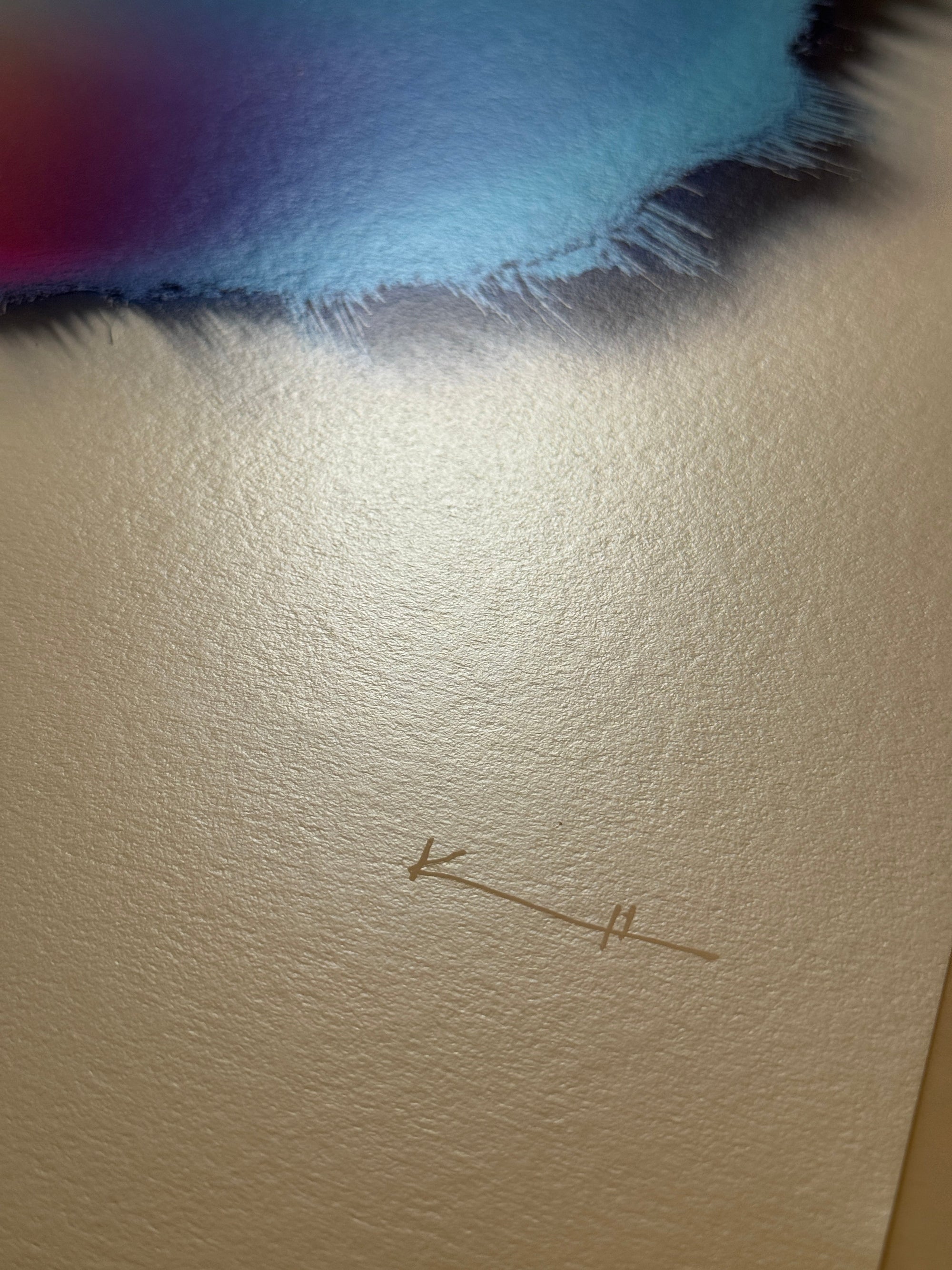 IMPACT 0017, close crop of blank cream paper below the disc, showing two small pencil marks, an arrow-like stroke and a short double tick, beside the blue and navy fringe at the top of frame.