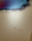 IMPACT 0017, close crop of blank cream paper below the disc, showing two small pencil marks, an arrow-like stroke and a short double tick, beside the blue and navy fringe at the top of frame.