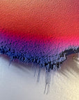 IMPACT 0017, close crop of the disc's lower edge where a red field deepens to magenta and purple before fraying into blue-black threads that drip down onto the plain cream paper below.