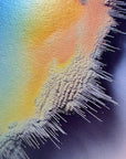 IMPACT 0018, close-up of the ragged fringe where a blue-green field meets yellow-orange and pink, the torn edge showing a fine black-and-white woven texture with drip marks trailing down.