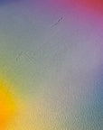 IMPACT 0018, close-up of the blank cream paper beside the disc, showing its fine texture under a soft blue, purple, pink, yellow, and green colour wash, with a couple of faint diagonal scratch lines.