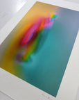 What Comes Back by Atelier Kalle Hellzén, hand-signed and numbered Limited Edition of 5, photographed at an angle on a light surface to show the weight and grain of the sheet. The figure sits in a teal-to-orange field; the signed "KH" mark is visible on the lower deckle edge. Giclée on handmade kozo washi.