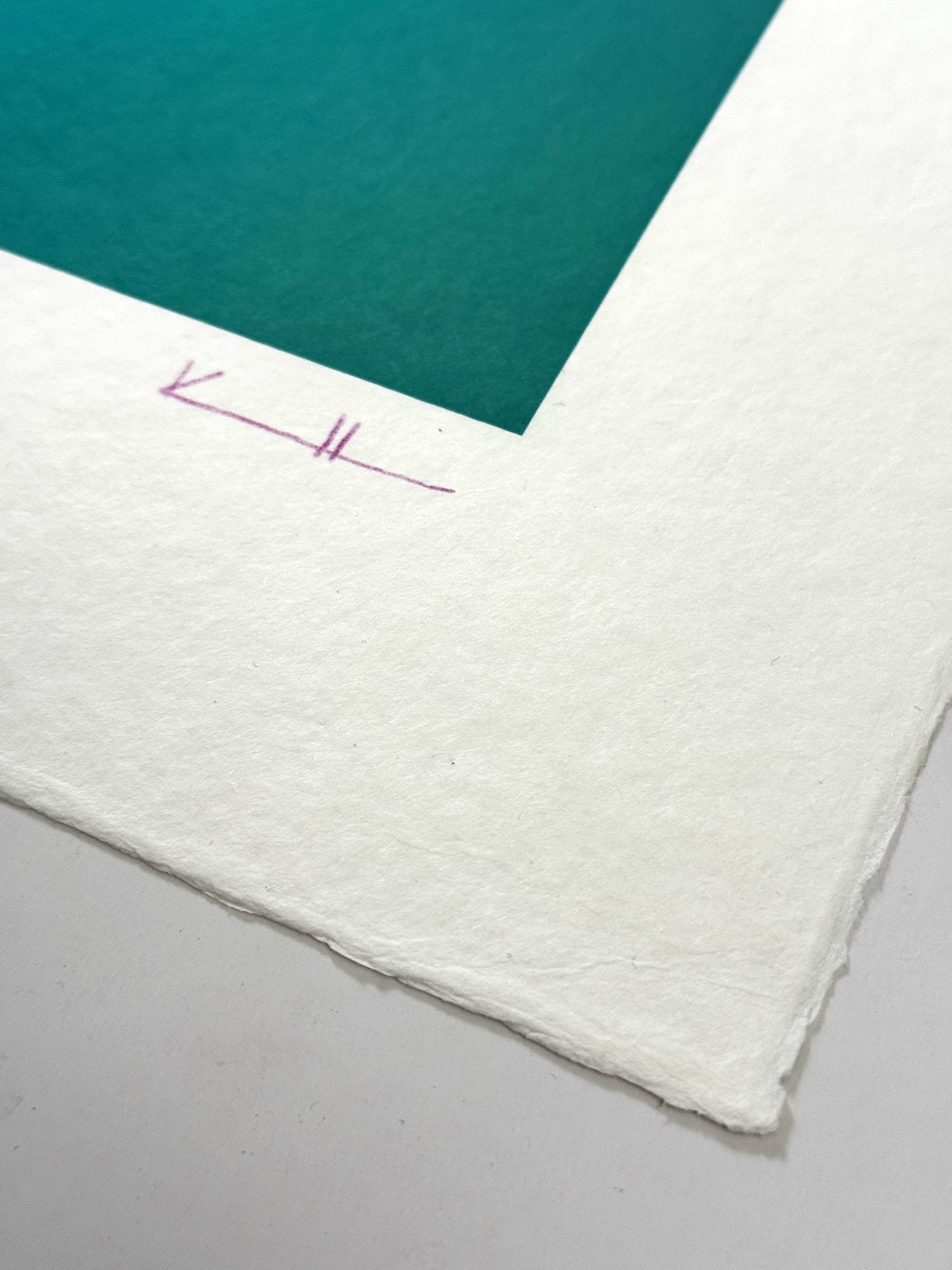 Detail of What Comes Back by Atelier Kalle Hellzén showing the artist's hand-drawn "KH" signature in pink on the lower deckle edge of the sheet, beside a band of teal from the print. Hand-signed and numbered Limited Edition of 5 on handmade kozo washi.